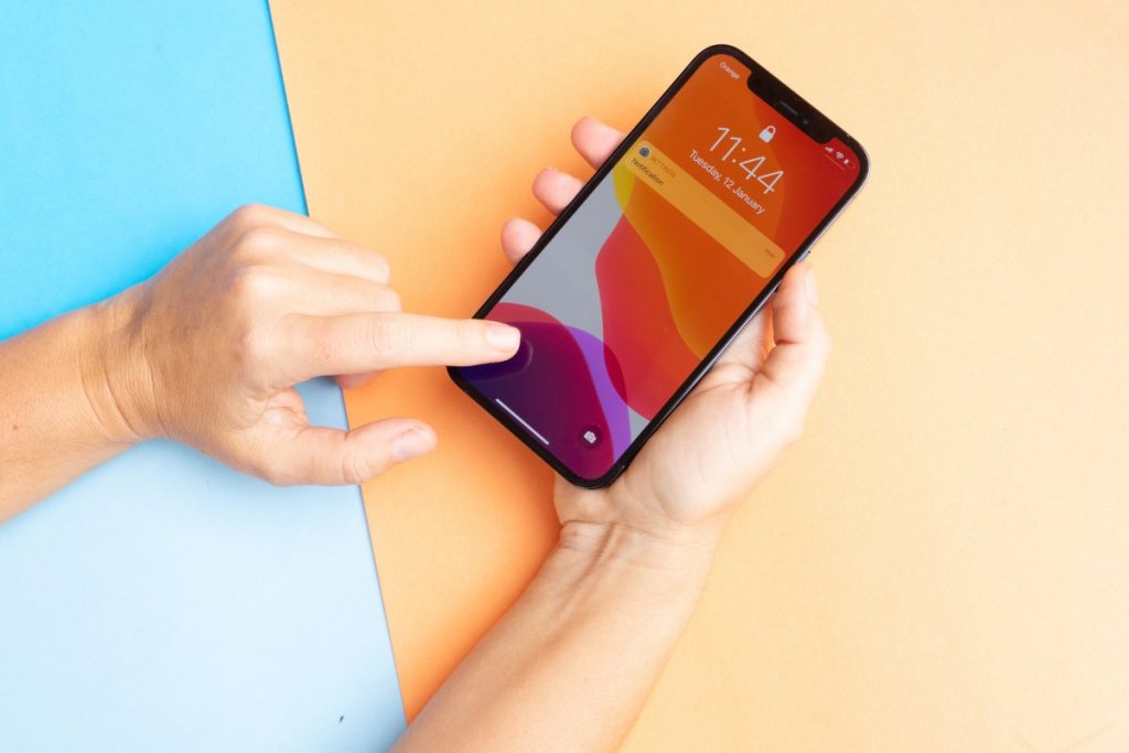 A hand holding a smartphone showing the lock screen with a notification at 11:14 AM. Background is split into blue and orange sections.